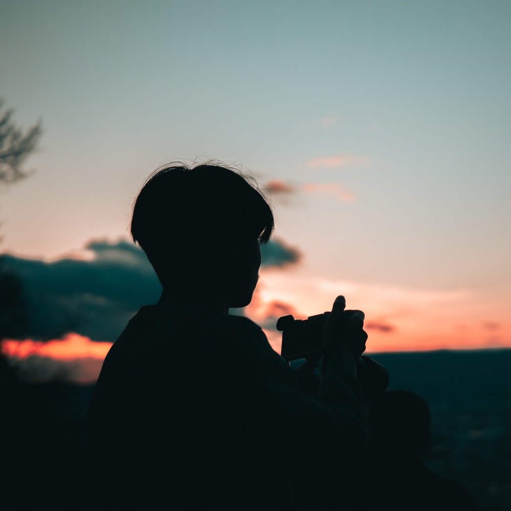 Caleb silhouetted against a colourful sunset while holding a camera