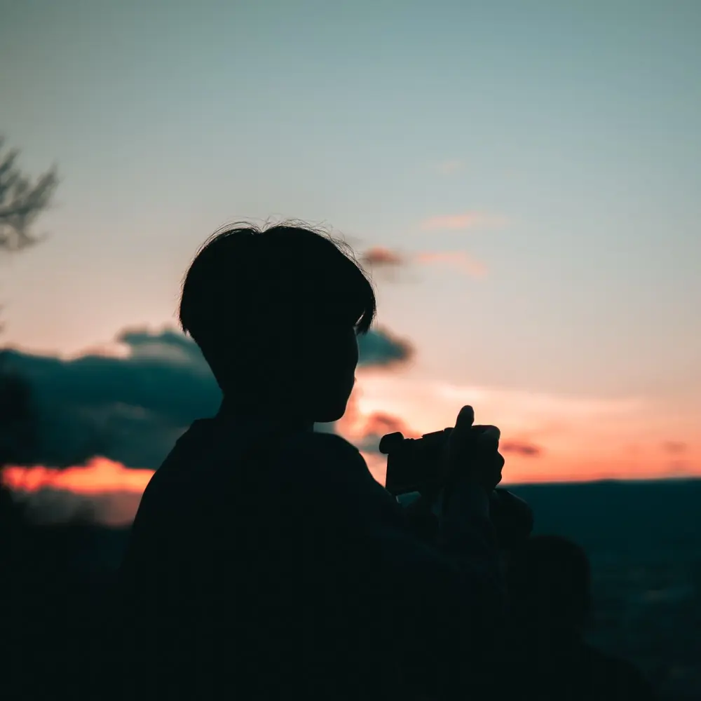 Caleb silhouetted against a colourful sunset while holding a camera