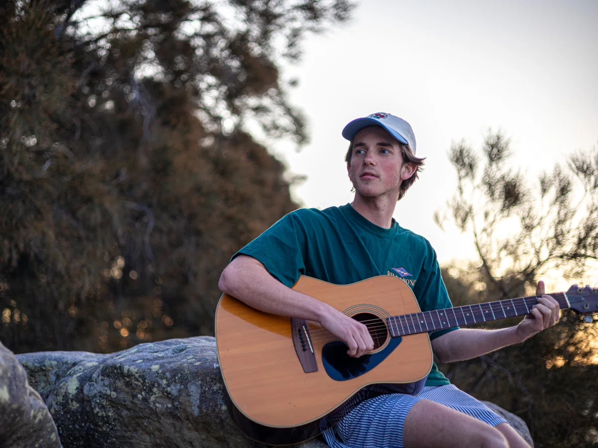 Musician seated outdoors with an acoustic guitar