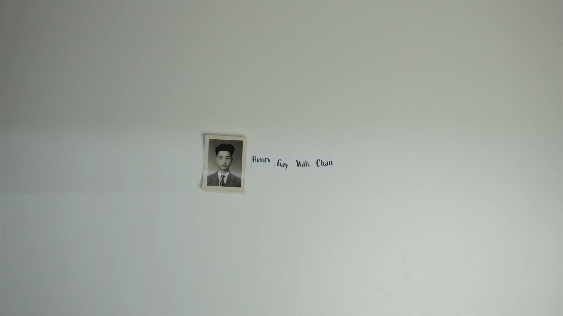 Henry Chan video still with a portrait and name on a wall