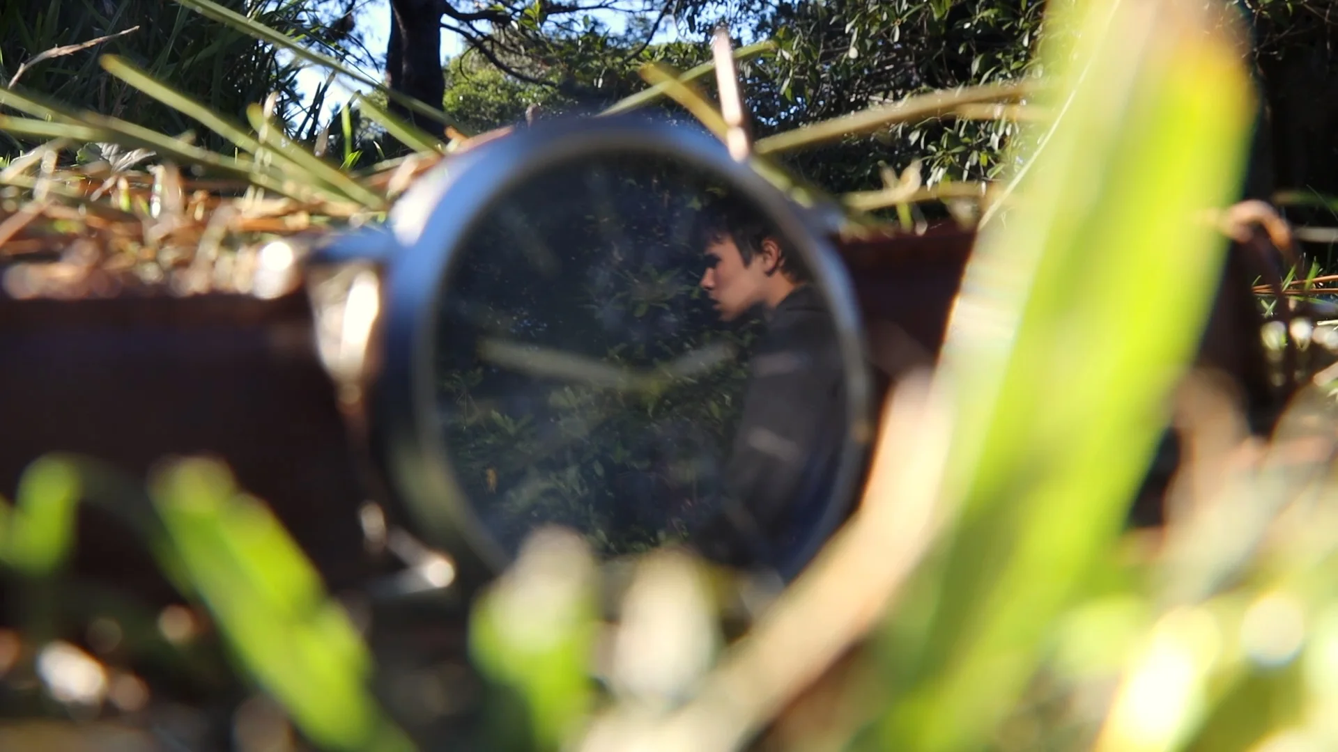 A person reflected in a circular mirror among green foliage
